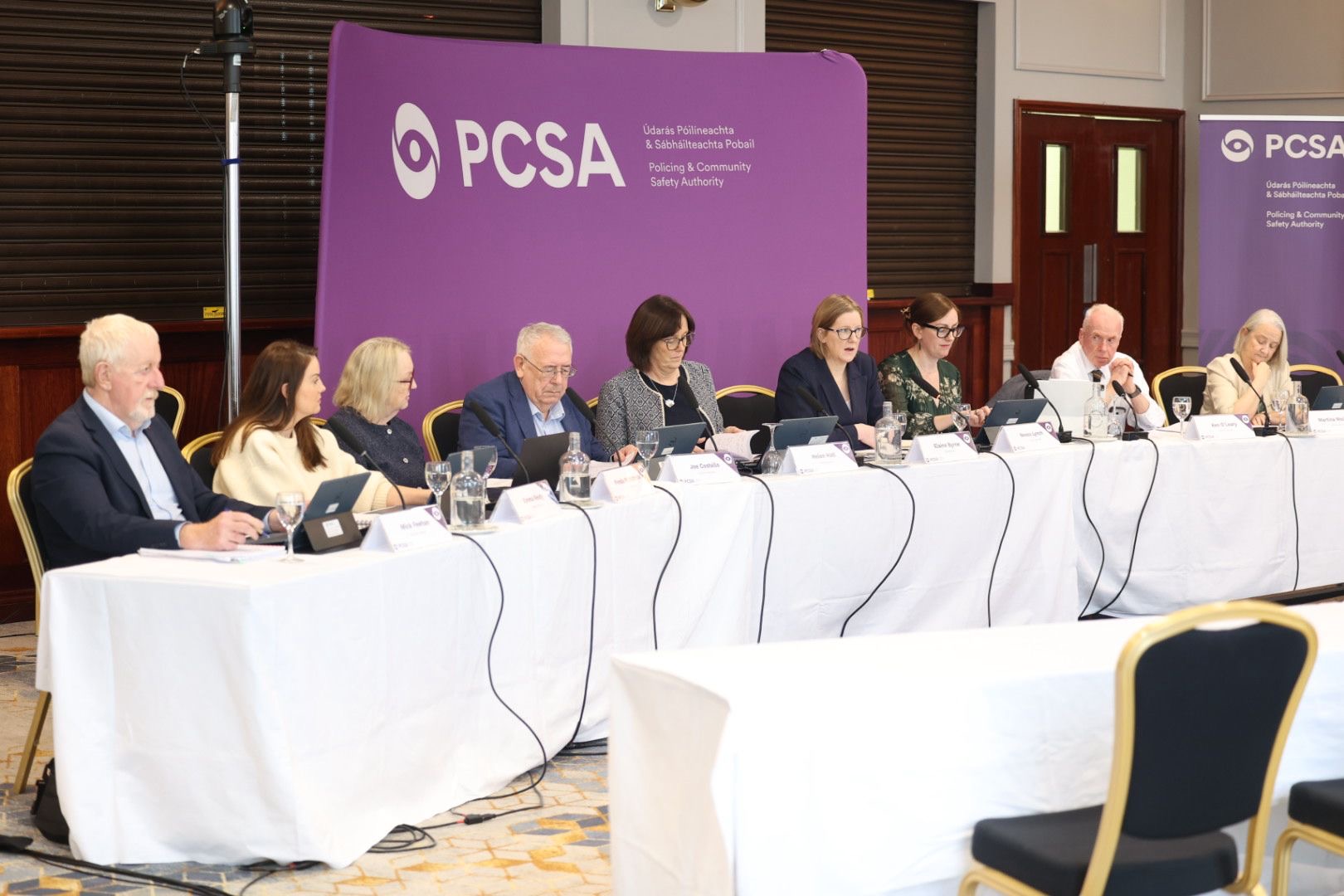 Nine members of the PCSA Authority sit at a desk in front of a purple