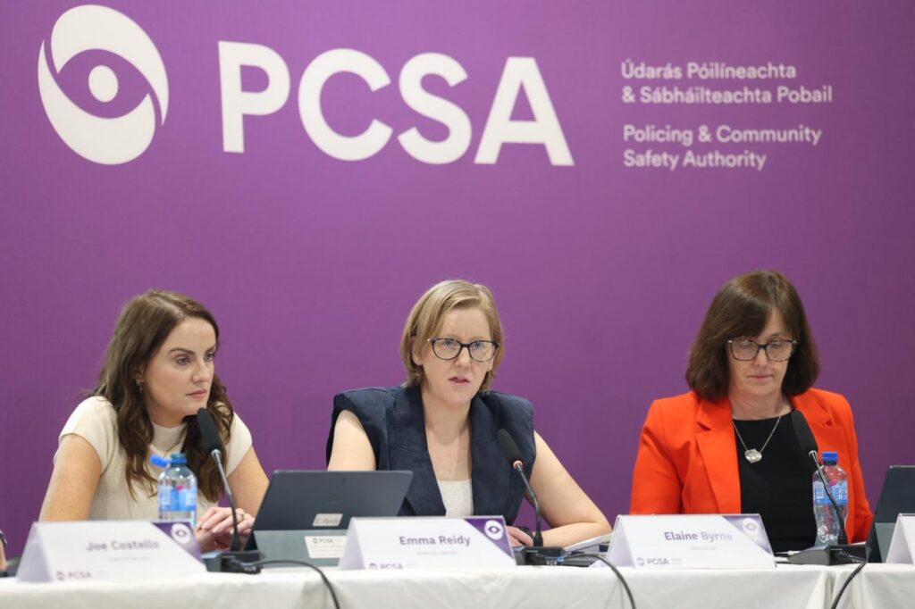 Three women sit at a table in front of a purple banner