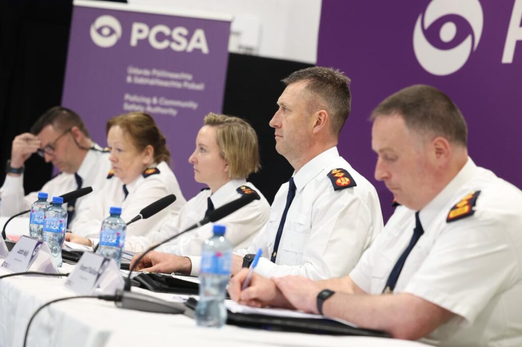 Five senior police officers sit at a table in front of a purple banner