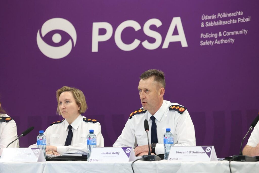Two senior police officers, a man and woman, sit at a table in front of a purple banner with PCSA on it