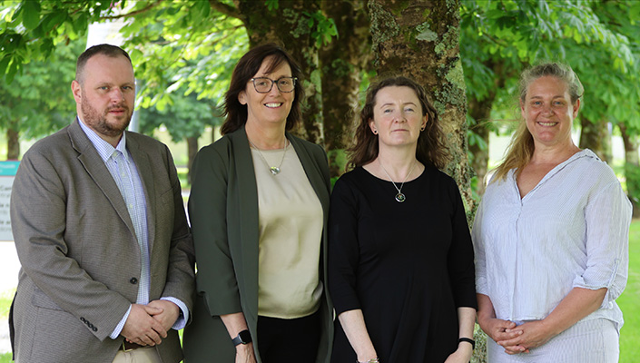 Three women and a man pose in front of a tree for an official photograph to launch a research a report