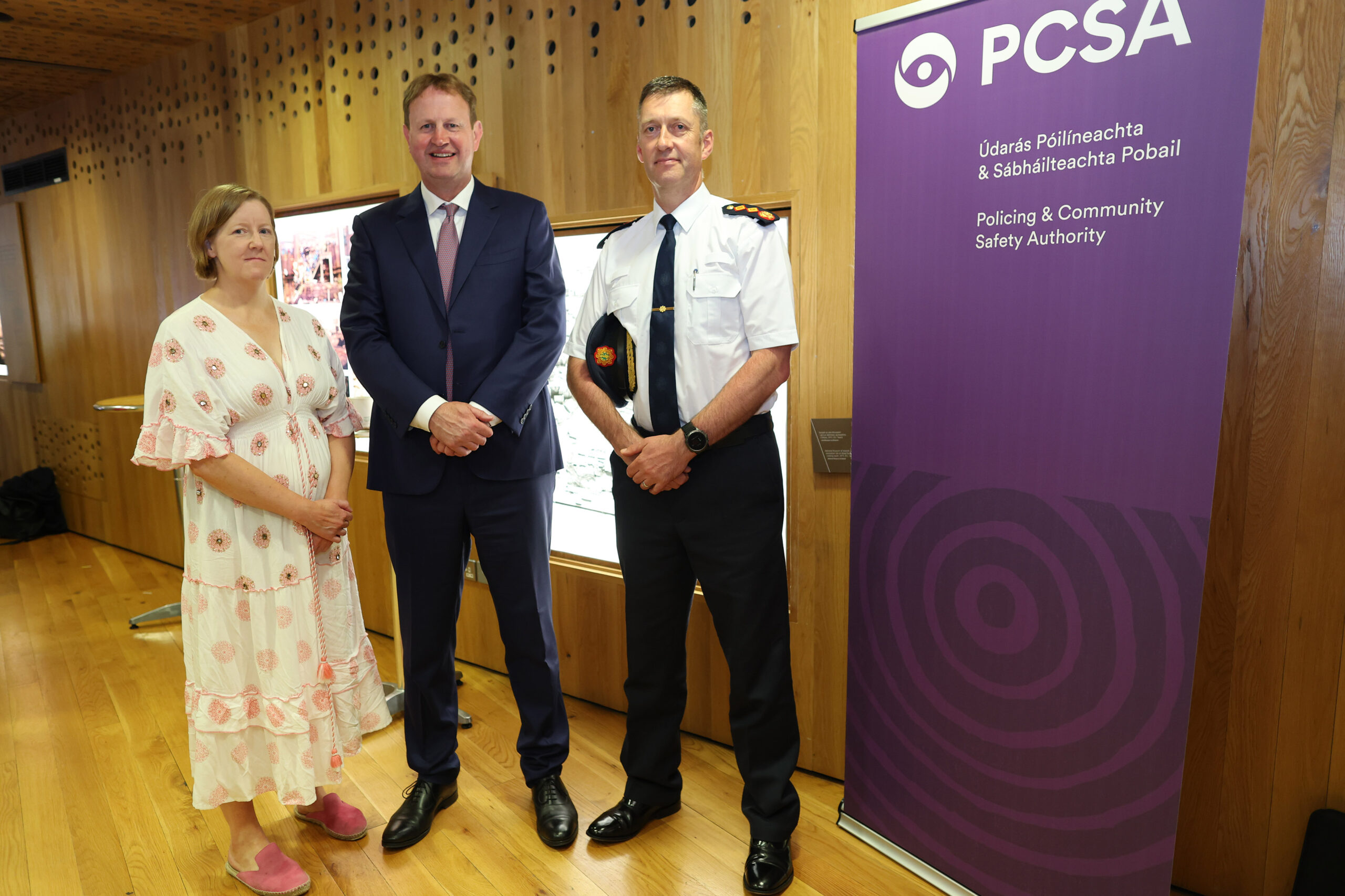 A woman in a white dress stands to the left of a man in a navy suit and a senior police officer in navy trousers and a white shirt